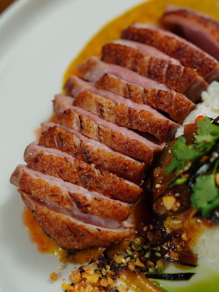 Close-up of tender duck breast slices with a rich sauce and garnished rice, showcasing food photography.