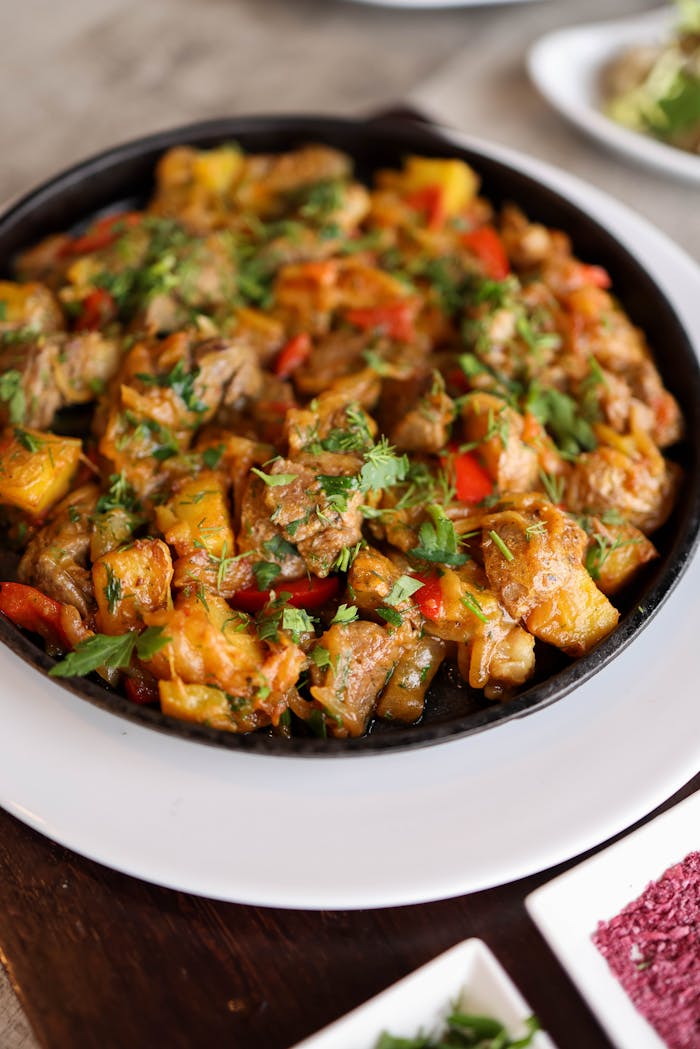 A flavorful meat stew with vegetables served in a white dish, garnished with herbs.