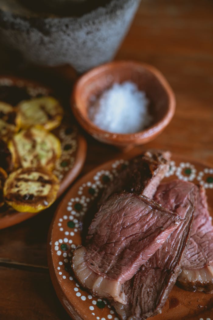 Sliced steak served with grilled vegetables and sea salt on rustic plates.